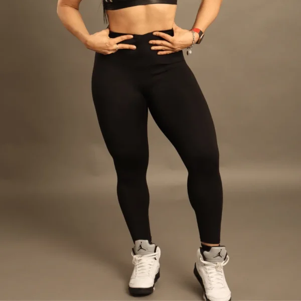 Mujer usando leggings deportivos negros de cintura alta con efecto moldeador y tela técnica para gimnasio