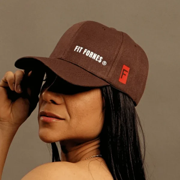 Mujer usando una gorra deportiva marrón de Fit Fornes con logotipo blanco bordado en el frente y detalle rojo lateral.
