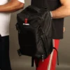 mochila-tactica-gym-negra-fit-fornes.jpg Un hombre sosteniendo en su brazo y usando camiseta negra deportiva carga una mochila táctica negra de alta resistencia con el logotipo de Fit Fornes.