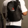 mochila-tactica-gym-negra-fit-fornes.jpg Un hombre de espaldas con una camiseta blanca deportiva carga una mochila táctica negra de alta resistencia con el logotipo de Fit Fornes.