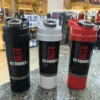 Tres shakers mezcladores Fit Fornes en colores negro, blanco y rojo sobre un mostrador de granito en una tienda de suplementos.