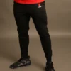 Primer plano de las piernas de un hombre usando pantalones jogger negros ajustados con el logotipo rojo de Fit Fornes en el muslo derecho.