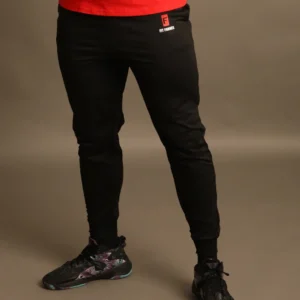 Primer plano de las piernas de un hombre usando pantalones jogger negros ajustados con el logotipo rojo de Fit Fornes en el muslo derecho.
