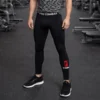 Hombre en el gimnasio usando leggings de compresión negros Pro Combat con el logotipo rojo de Fit Fornes en el tobillo y banda elástica en la cintura.