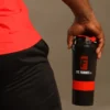 Mano de un atleta sosteniendo un shaker mezclador negro con tapa roja y el logotipo oficial de Fit Fornes.
