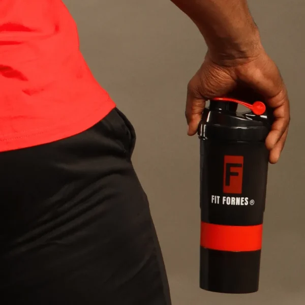 Mano de un atleta sosteniendo un shaker mezclador negro con tapa roja y el logotipo oficial de Fit Fornes.